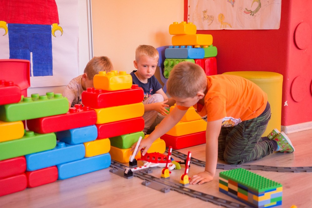 Tri deti predškolského veku sa hrajú s veľkou lego stavebnicou.