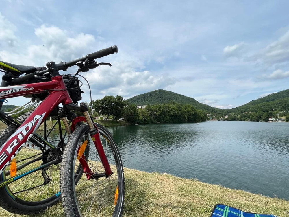 Dva horské bicykle zaparkované pri jazere s výhľadom na zalesnené kopce.