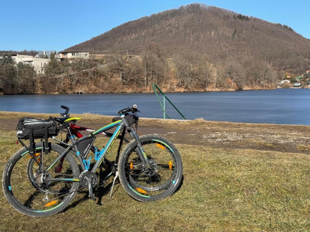 Dva bicykle opreté o seba na brehu jazera s výhľadom na okolité domy a hory.