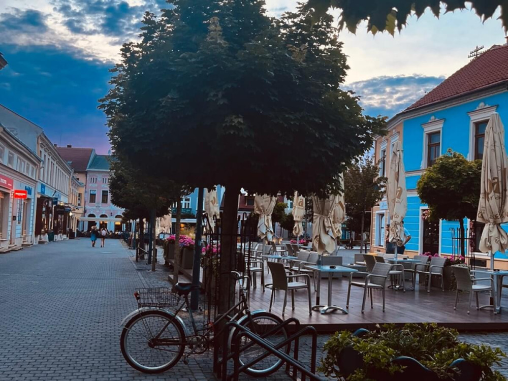Námestie mesta s kaviarňou a stromami o ktoré je opretý bicykel.