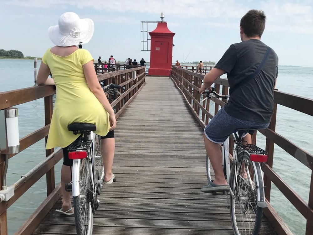 Muž a žena na bicykloch na drevenom móle vedúcom k červenému majáku nad jazerom.