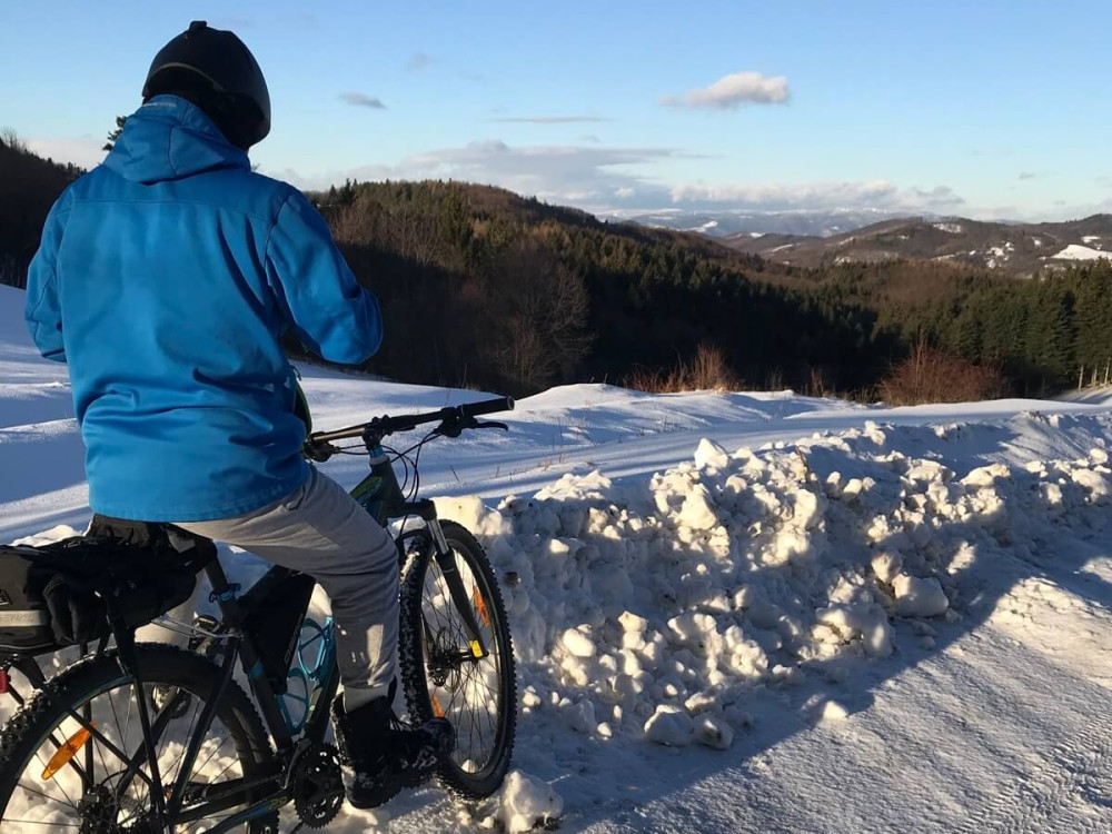 Muž na bicykli v zime na snehu s výhľadom na hory.