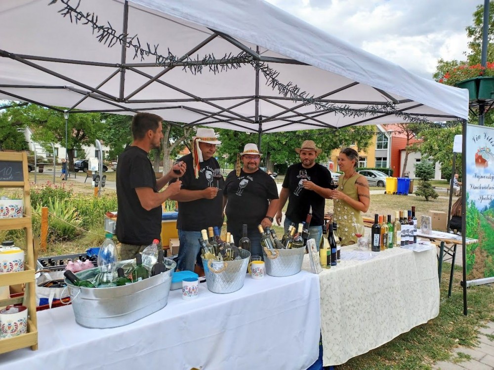 Štyria muži a žena v stánku predávajú rôzne druhy svojich vín