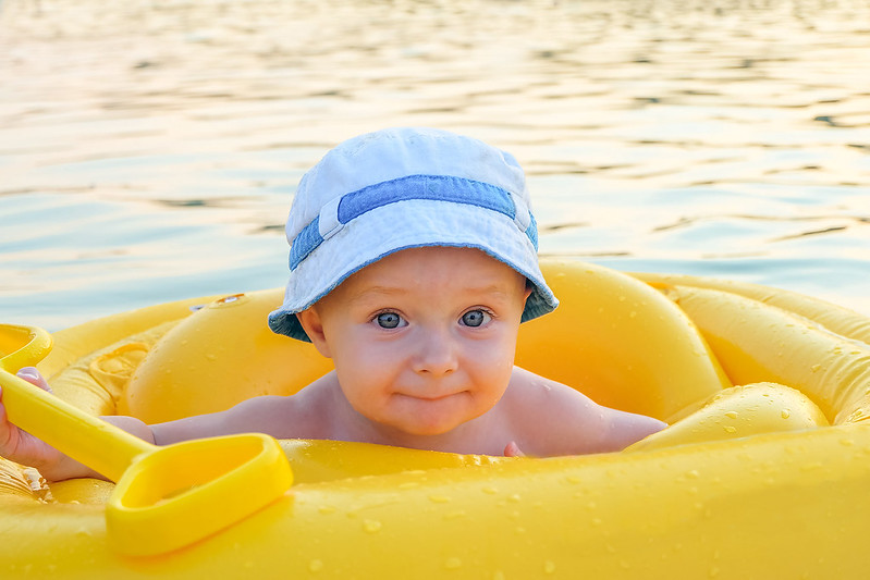 Dieťa v modrej kúpacej čiapke a žltom kolese vo vode