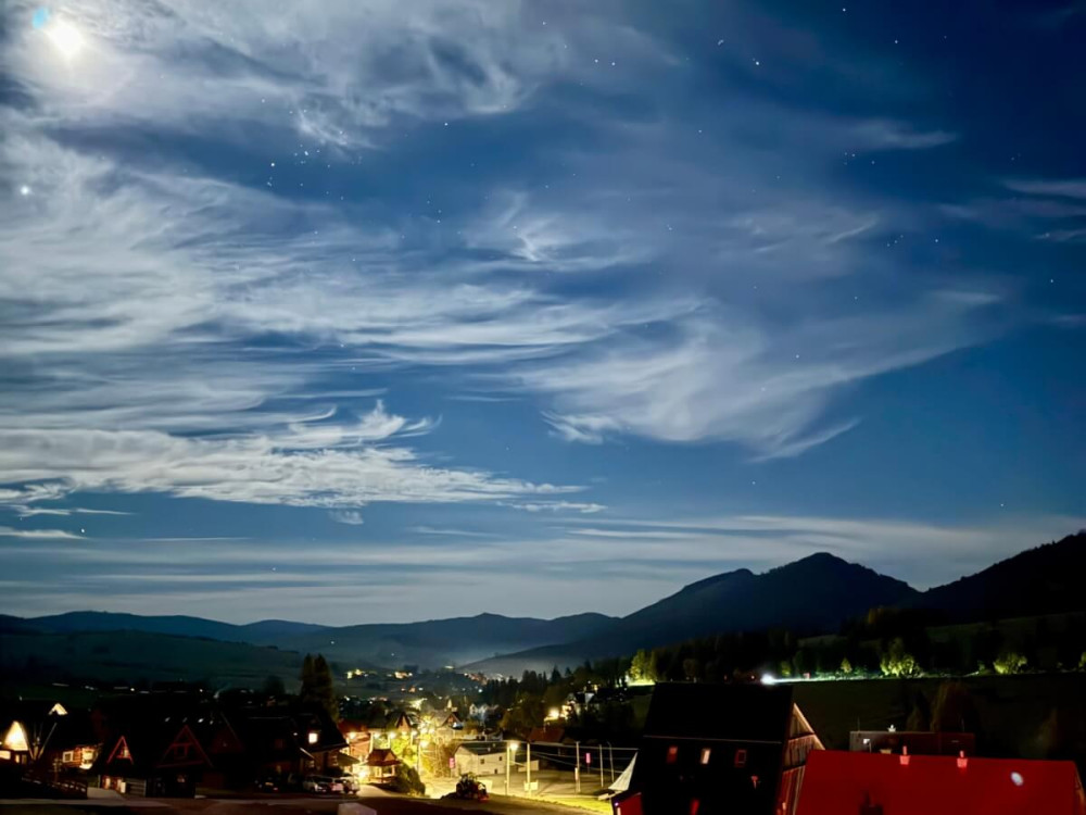 Nočná obloha s bielymi oblakmi nad vysvietenou dedinou.