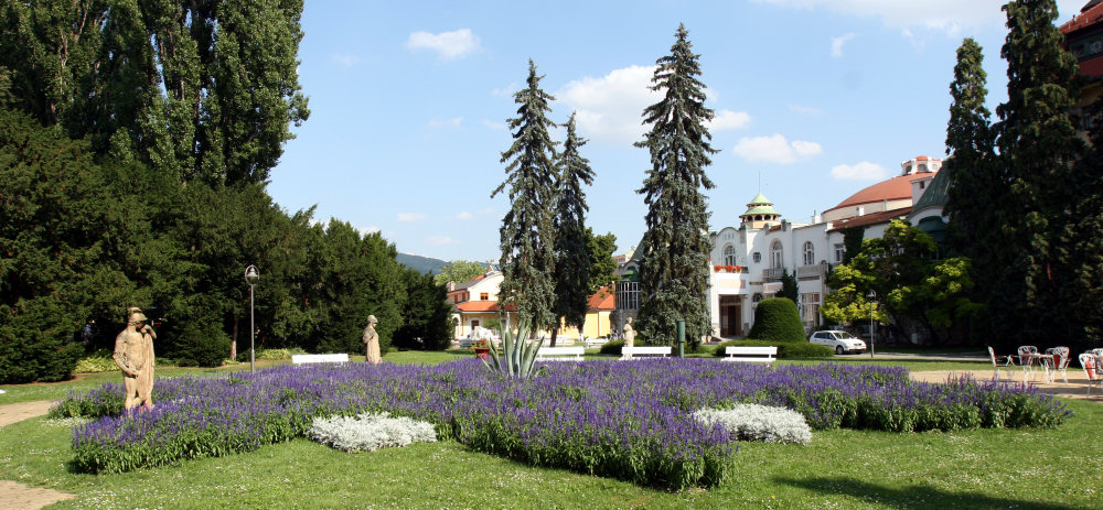 Pohľad na budovu Piešťanských kúpeľov, blízky park a drevené sochy